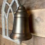 Brass medium-sized bell with rope hanger displayed on a farmhouse wood wall and vintage arch frame.