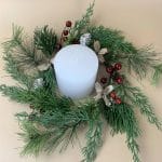 Round holiday candle wreath with pine needles, berries, and bow accents.
