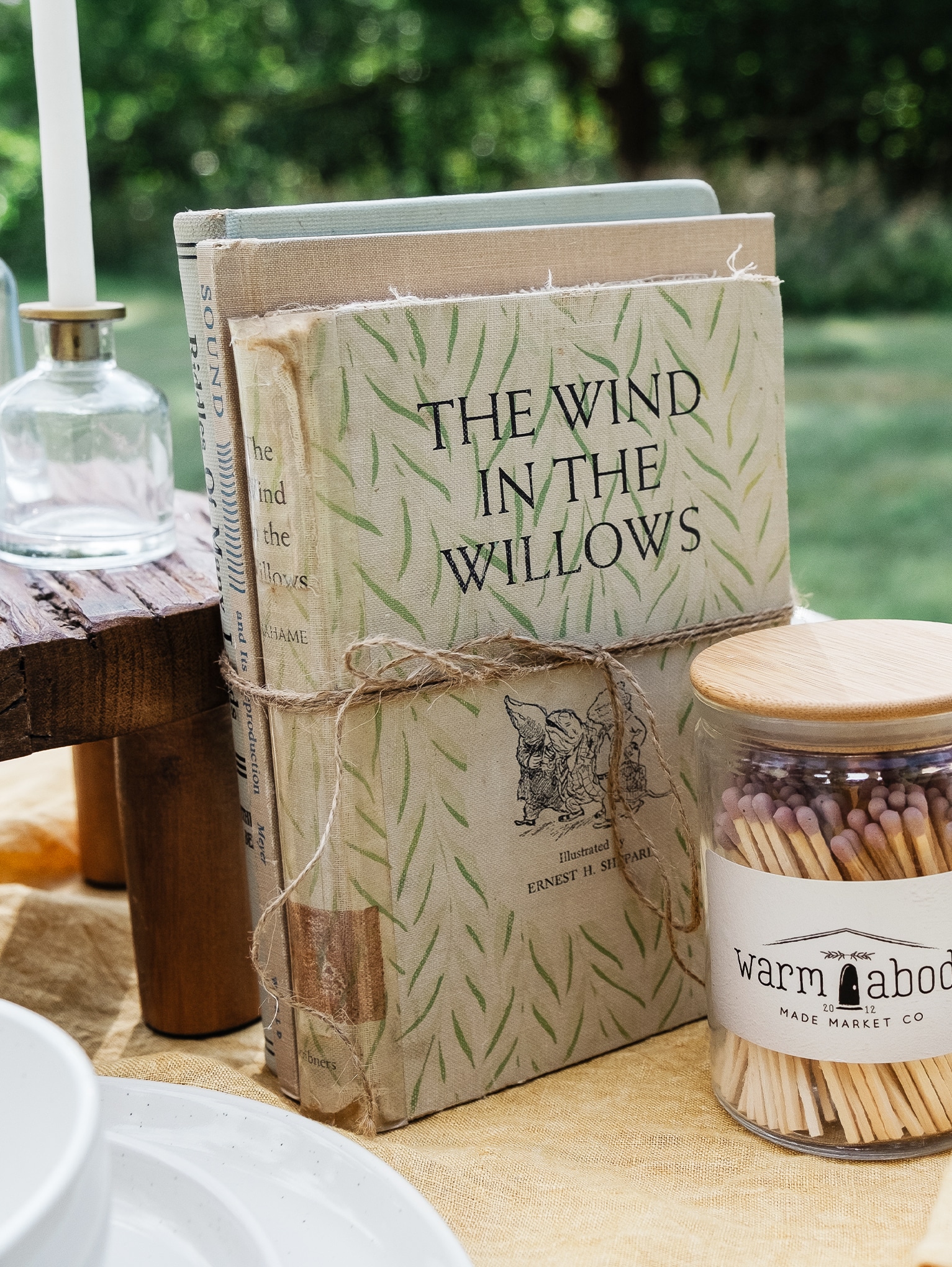Styled tabletop featuring vintage books, mauve matches, wood pedestal, glass taper holder, and white candle