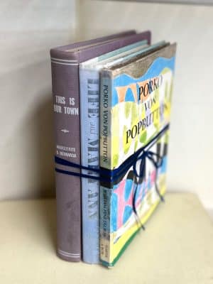 Three vintage hardcover books in eclectic colors, tied with navy ribbon, styled upright on a shelf
