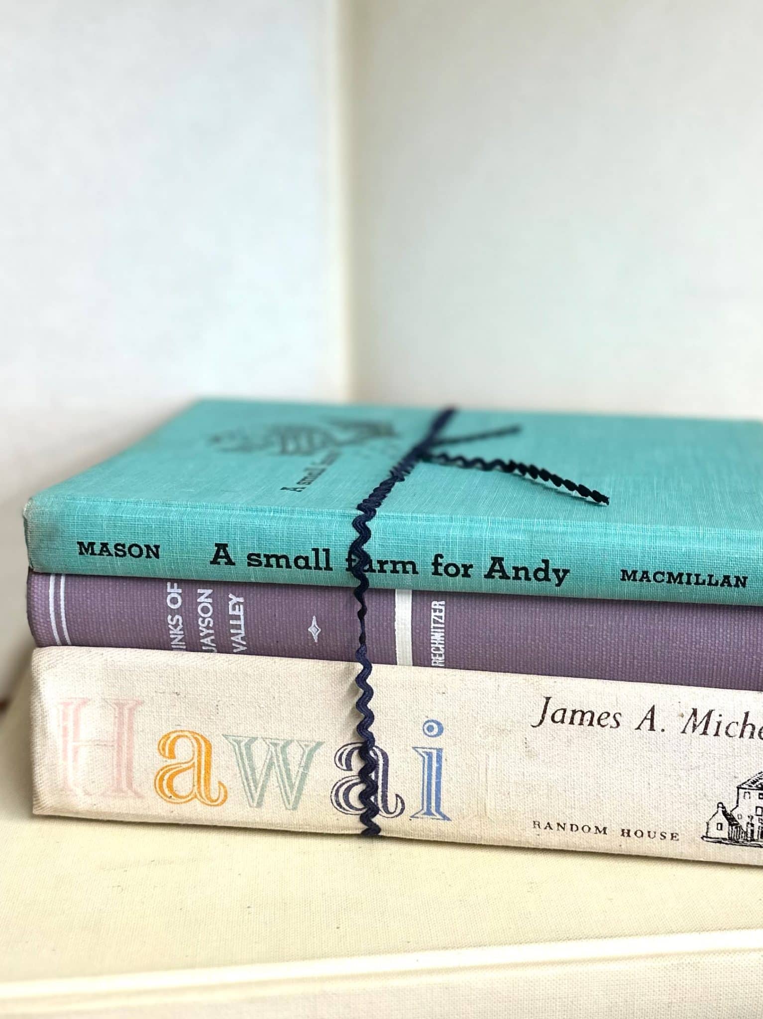Three vintage hardcover books in various colors with a ribbon tie