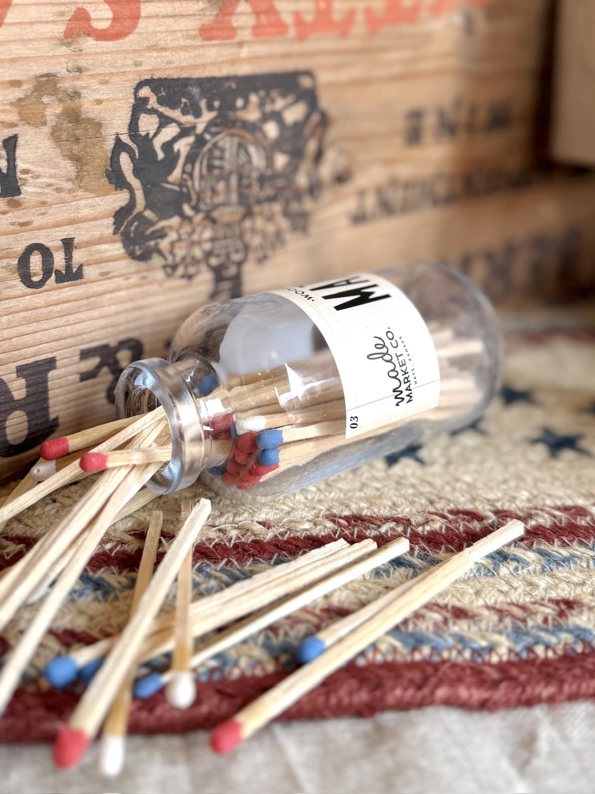 Mini glass apothecary jar of red, white, and blue matches tipped over on a patriotic table runner.