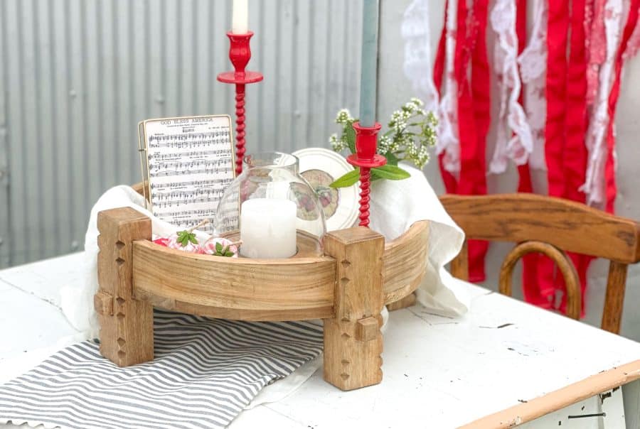 Wood Chakki Table styled with red corkscrew taper holders, white and blue taper candles, a glass hurricane candle holder, and patriotic sheet music in frame.