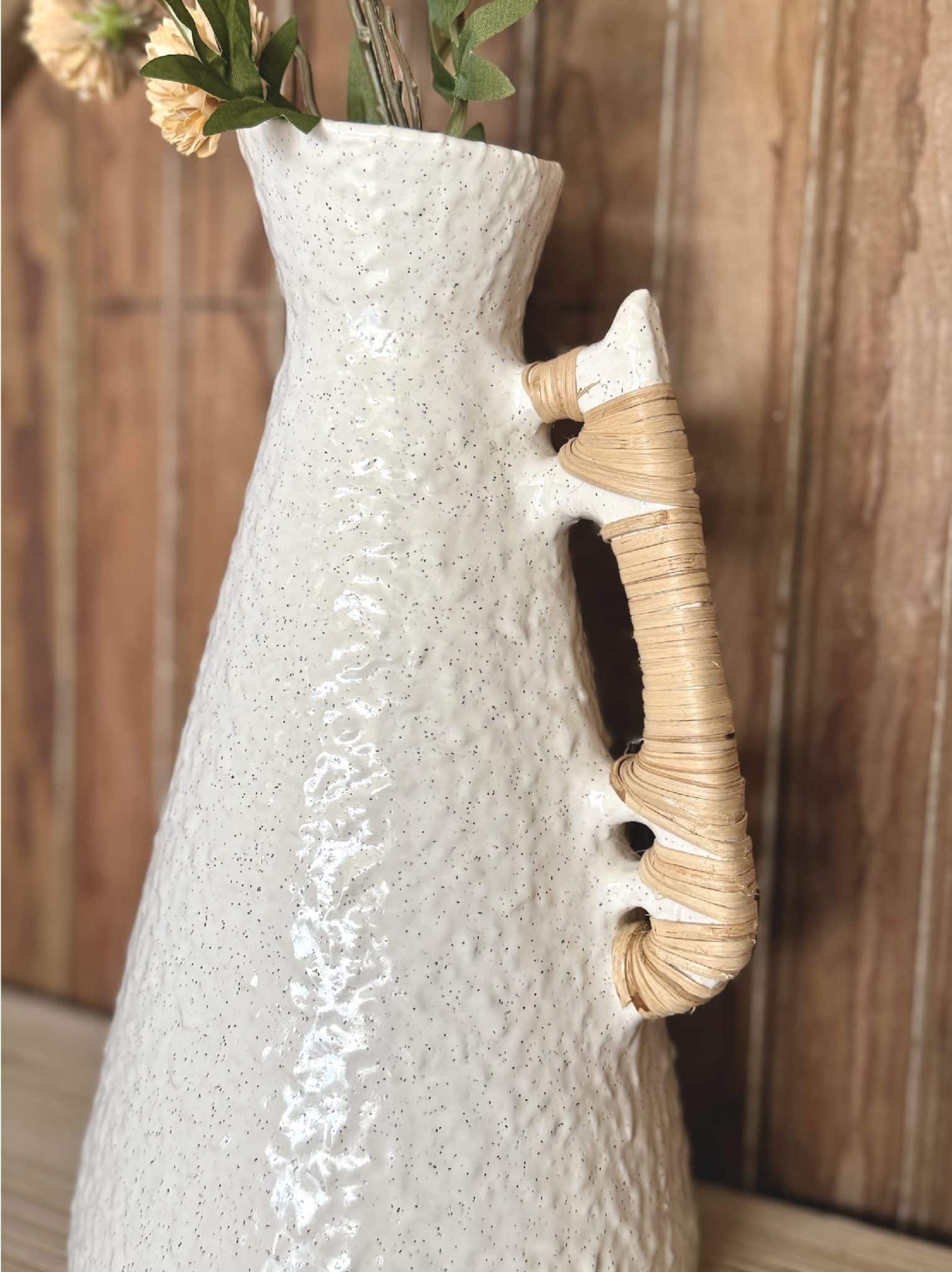 Detail of rattan-wrapped handle on white ceramic vase with textured glaze and organic silhouette.