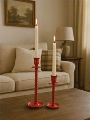 Two red corkscrew taper candle holders—one large and one small—styled on a coffee table with ivory taper candles lit, in a cozy living room setting.