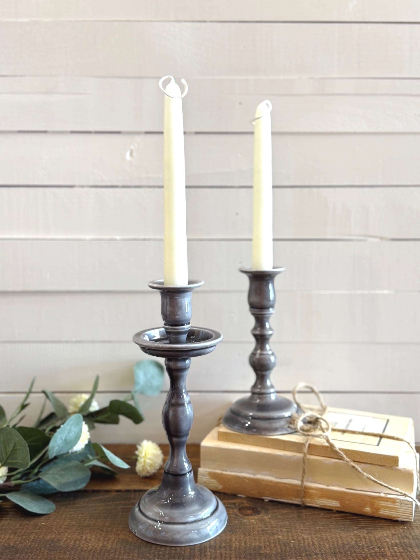 Front view of gray cast iron taper candle holders in two sizes, styled with books, florals, and cream candles.