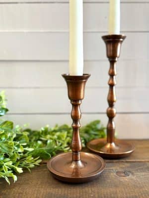 Copper taper candle holders with ivory taper candles, styled with greenery for a cozy, elegant setting.