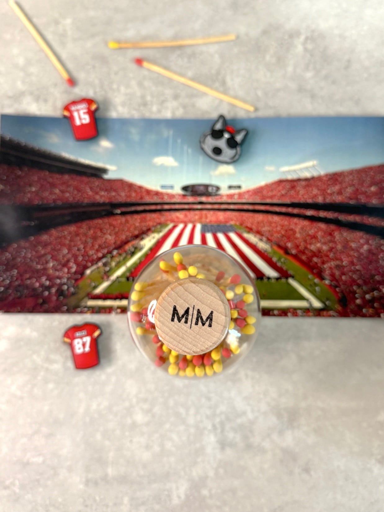 Top-down view of Victory Matches jar with MM logo cork, surrounded by KC-themed shoe charms