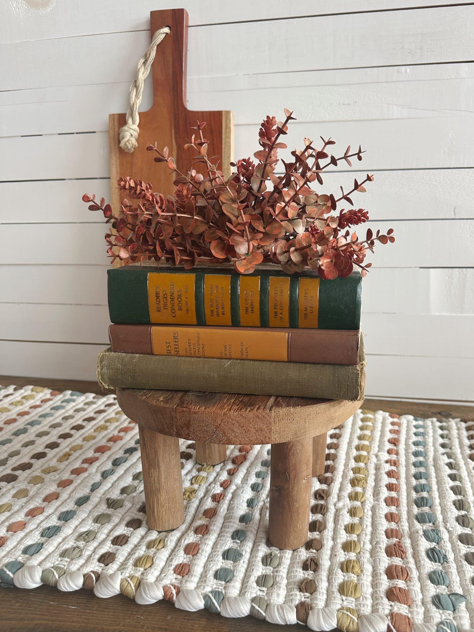 Round wood pedestal holding stacked vintage books in red, yellow, and green tones with fall florals
