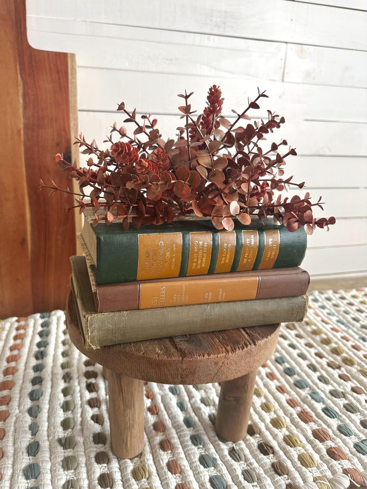 Close-up of decorative vintage book trio on wood pedestal with dried fall florals