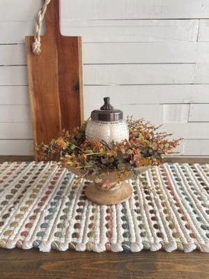 Glass pumpkin candle with lid in pedestal bowl surrounded by fall florals, styled in front of wood board