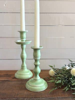 Mint taper candle holders styled with soft florals and greenery against a white shiplap background.