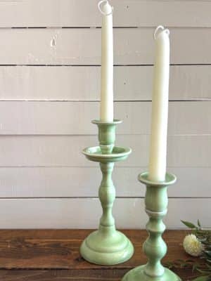 Side view of two mint enamel candle holders with elegant, curvy silhouettes and ivory taper candles.