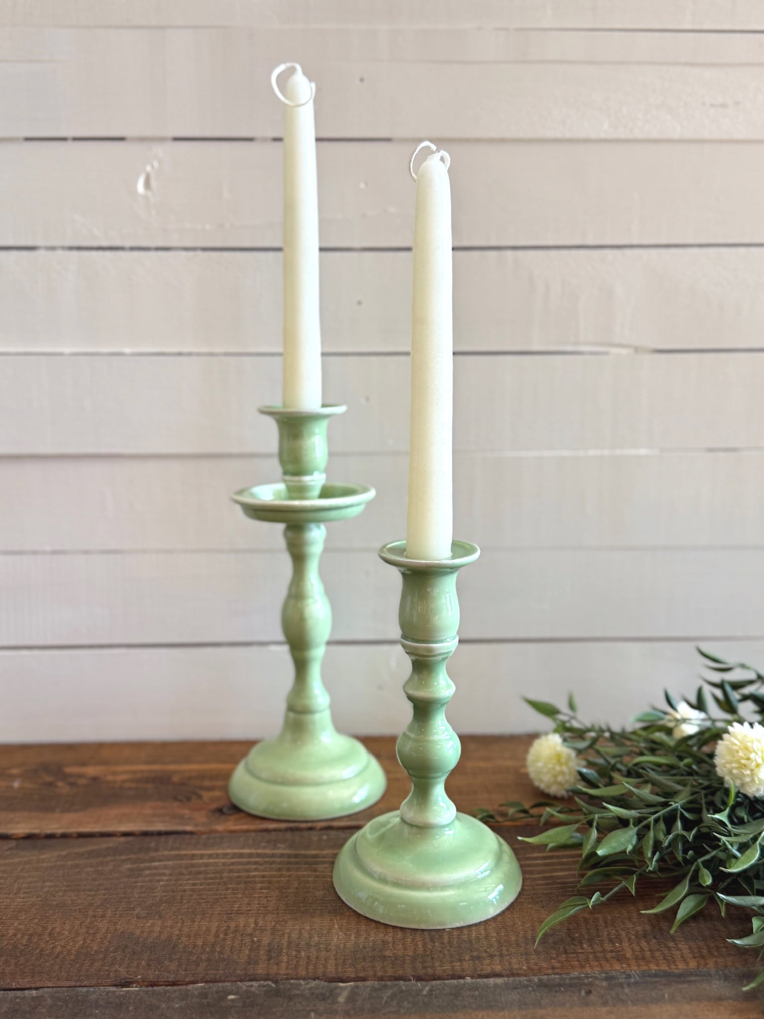 Close-up of mint taper holders in medium and small sizes holding ivory taper candles in front of a white wall.