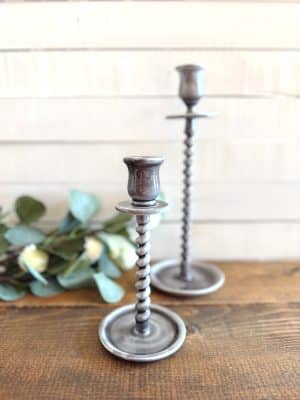 Gray taper candle holders shown without candles, styled on a wooden table with scattered eucalyptus.
