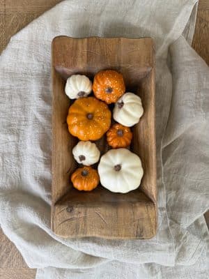 Small crafted wood dough bowl filled with mini white and orange pumpkins, styled on a light linen cloth.