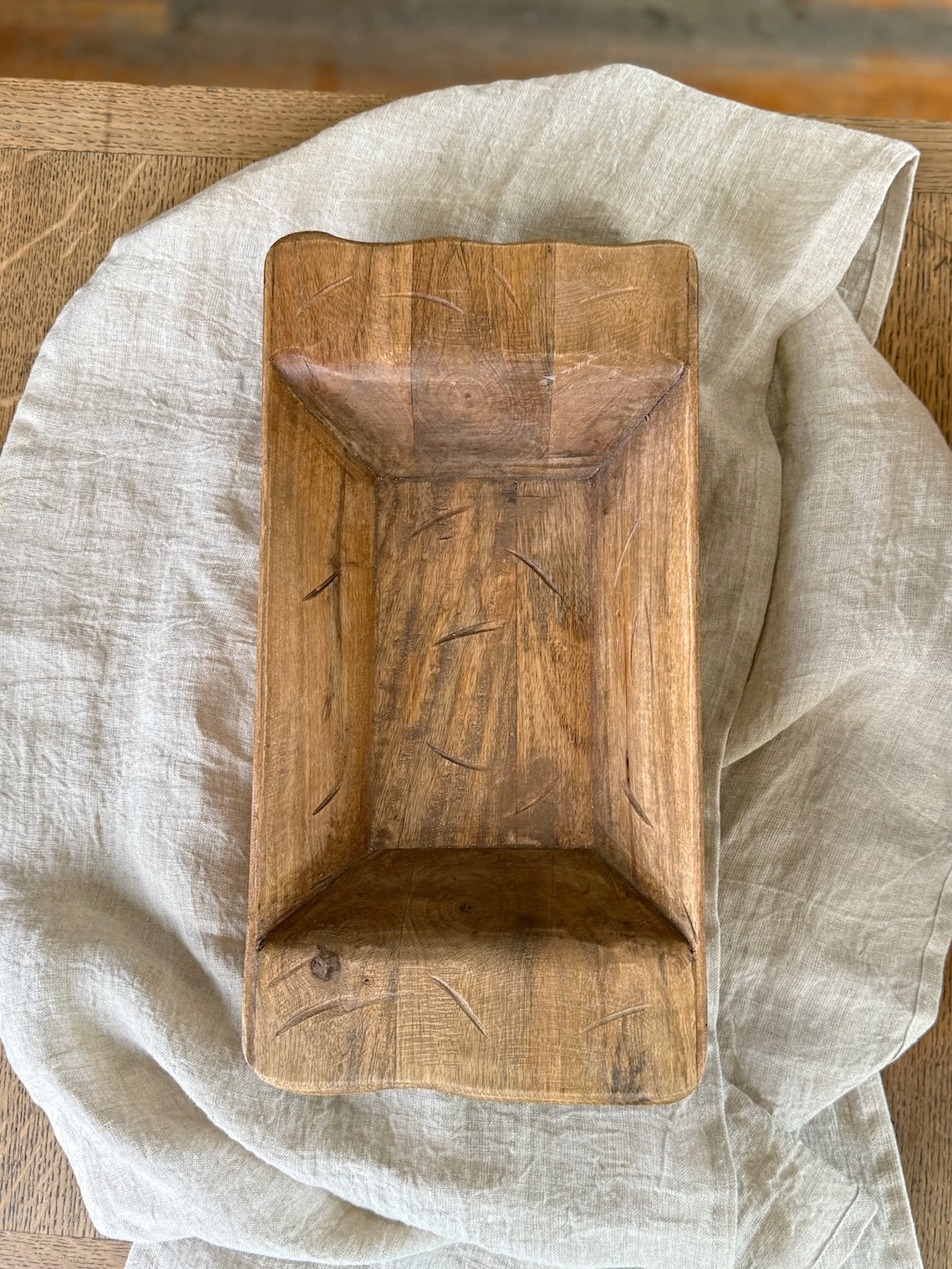 Hand-carved small wood dough bowl with natural grain and subtle carving marks, placed on a neutral linen cloth.