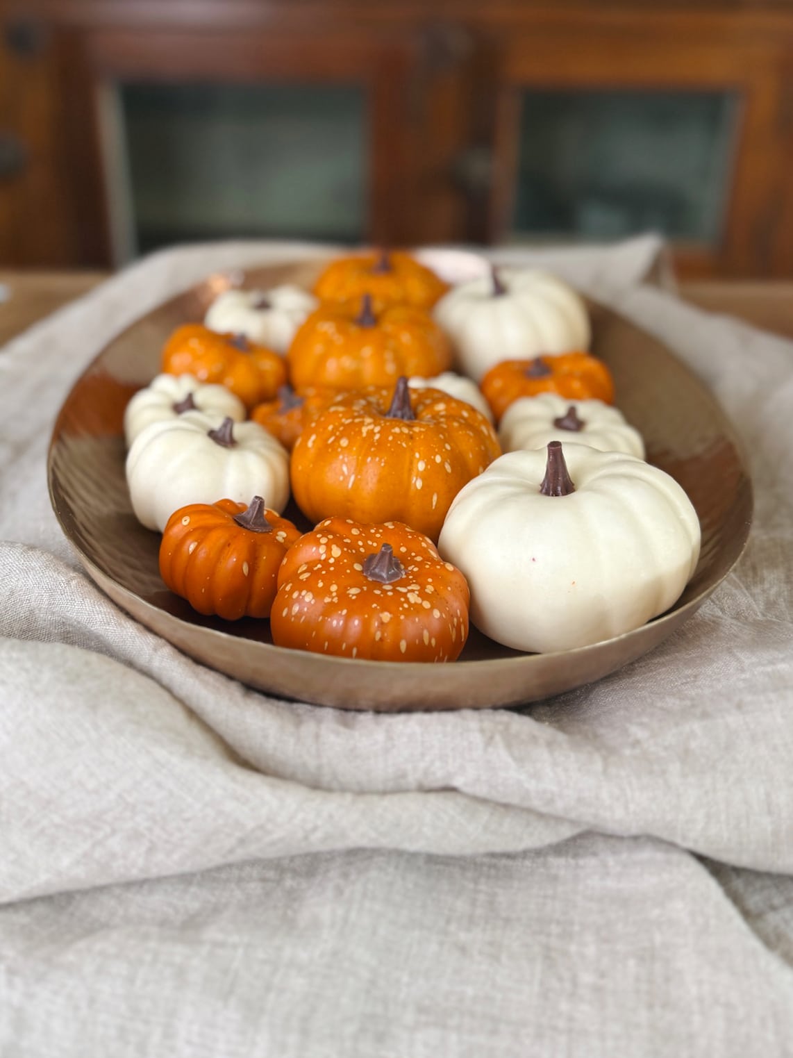 Side view of an oval hammered brass platter filled with white and orange pumpkins, styled with a soft beige linen cloth.