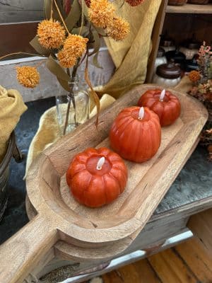 Large handcrafted wooden dough bowl with carved handles, styled with three pumpkin candles on a rustic table.