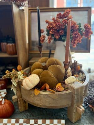 Traditional Indian-inspired wooden chakki pedestal holding pumpkins, candles, and autumn foliage.