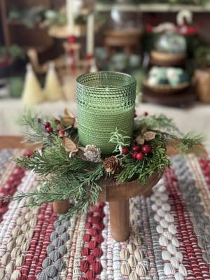 Round Wood Pedestal styled with a green candle and winter greenery on a red and neutral woven table runner.