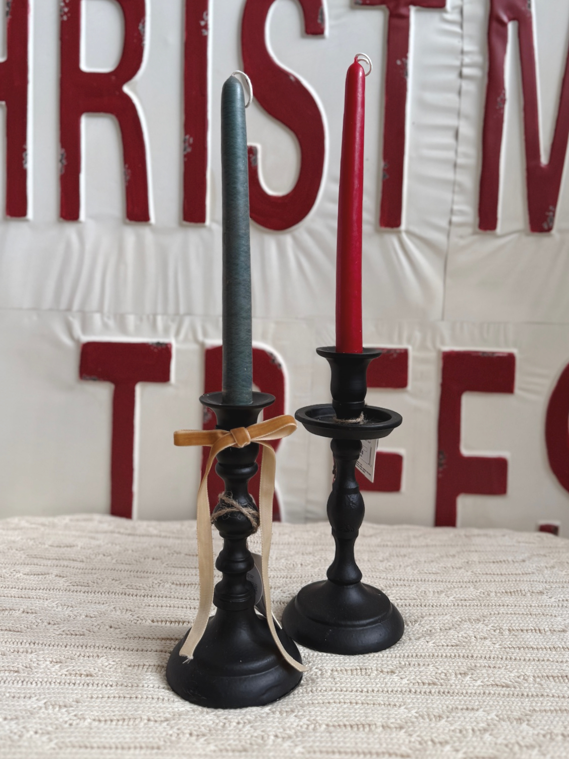 Black Empire Taper Candle Holders in small and medium sizes styled with Foliage and Fiery Evoke taper candles against a vintage red-and-white Christmas sign.