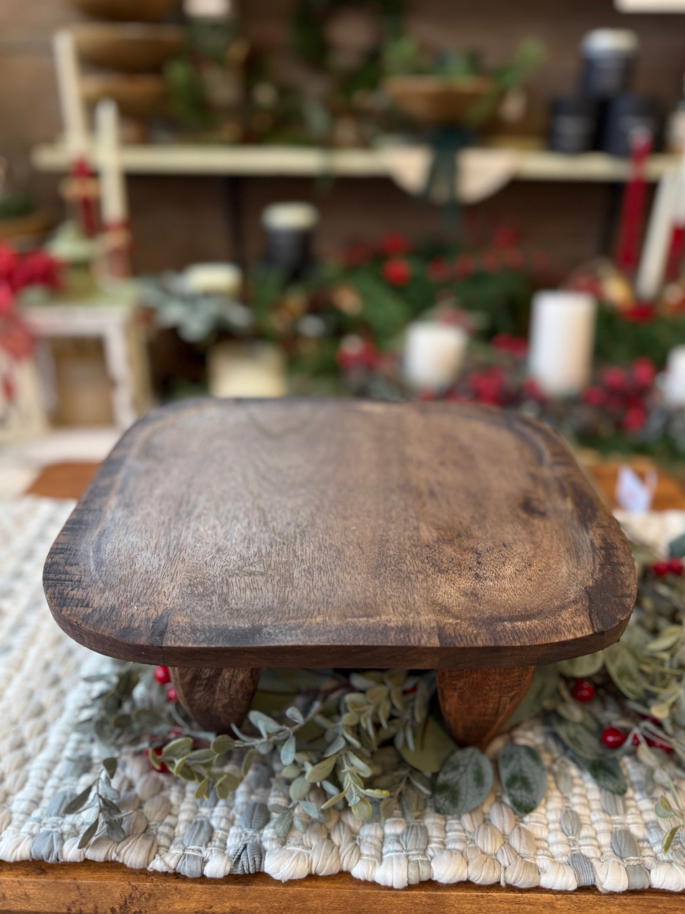 Front-angle view of the Square Wood Primitive Stool showing its rounded square top and chunky carved legs styled with greenery.