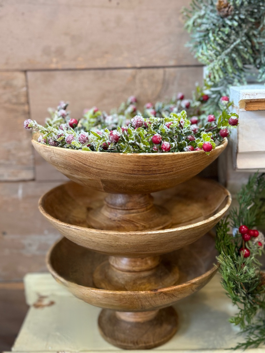 Classic wood pedestal bowl filled with frosted greenery and red berries, displayed on a wooden surface.