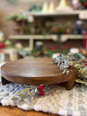 Large round found wood pedestal placed on a textured mat with greenery and red berries peeking under the front edge.large