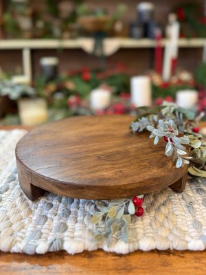 Found Wood Pedestal Medium shown from a straight-on front view, styled on a textured cream mat with winter greenery and red berries around the base.