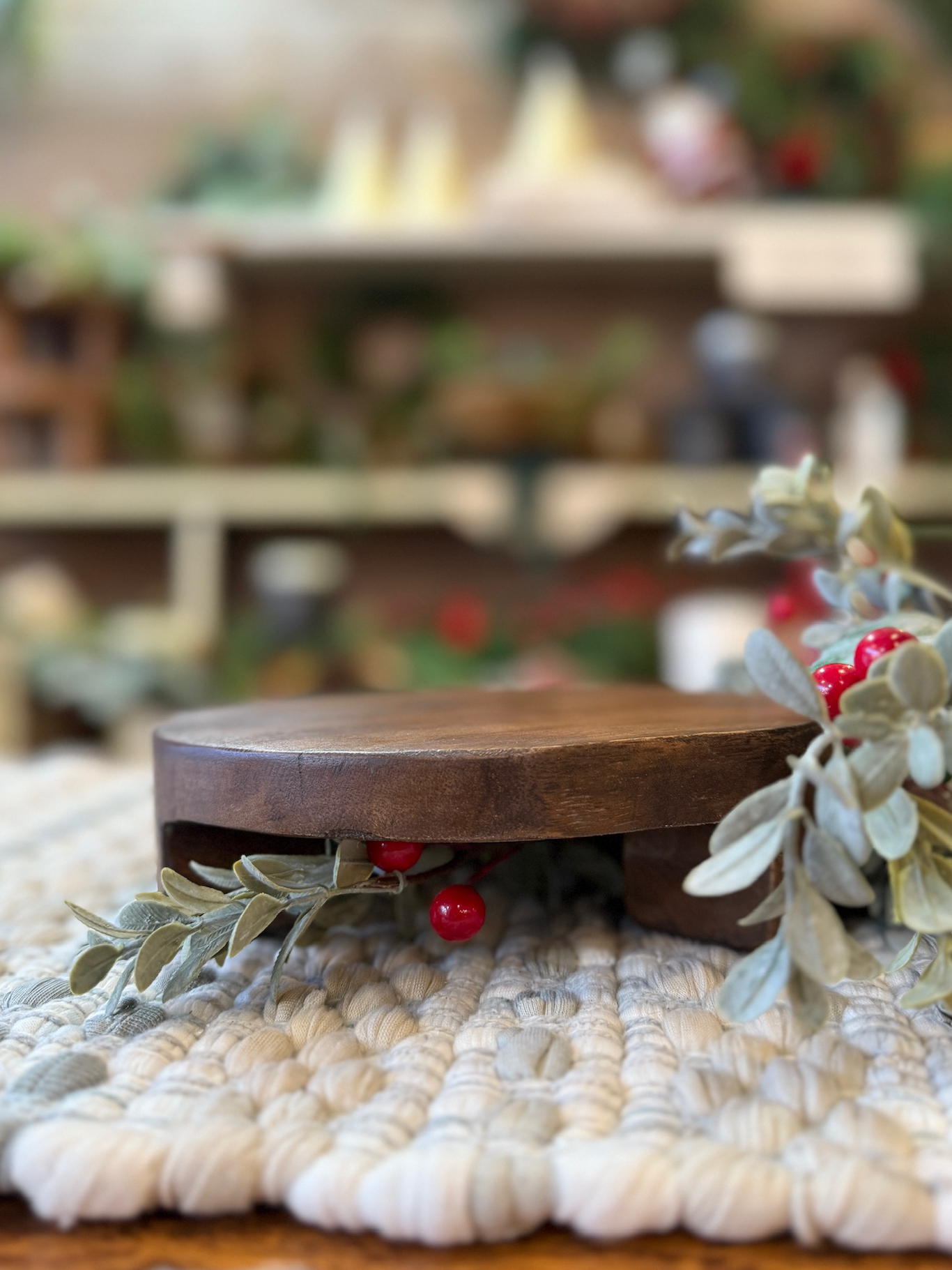 Found Wood Pedestal Small styled on a textured woven mat with winter greenery and red berries around the base.