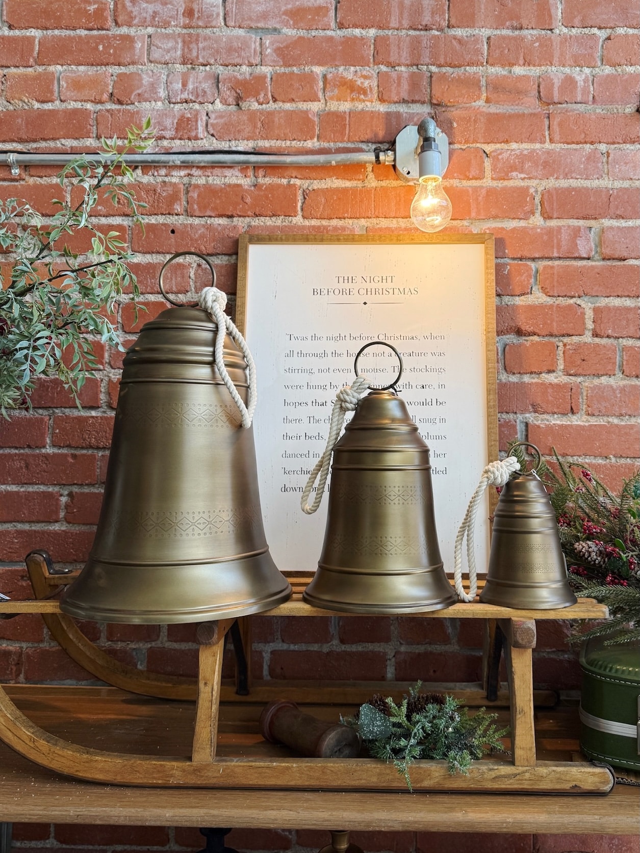 Antique Brass Bell Large, Medium, and Small displayed together on a rustic wooden sled against a brick backdrop.