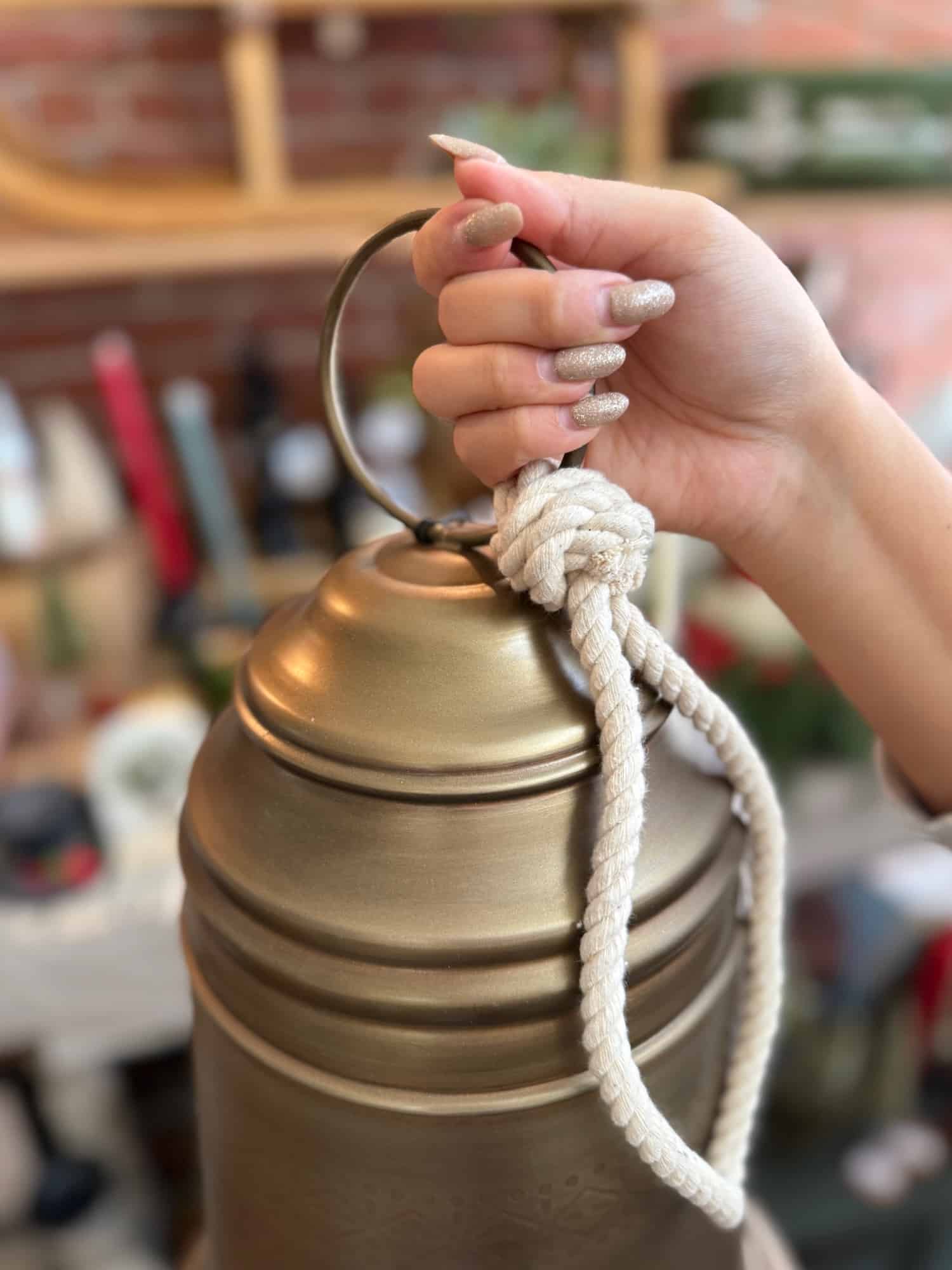 Close-up of the Antique Brass Bell Medium being held by its braided rope hanger.