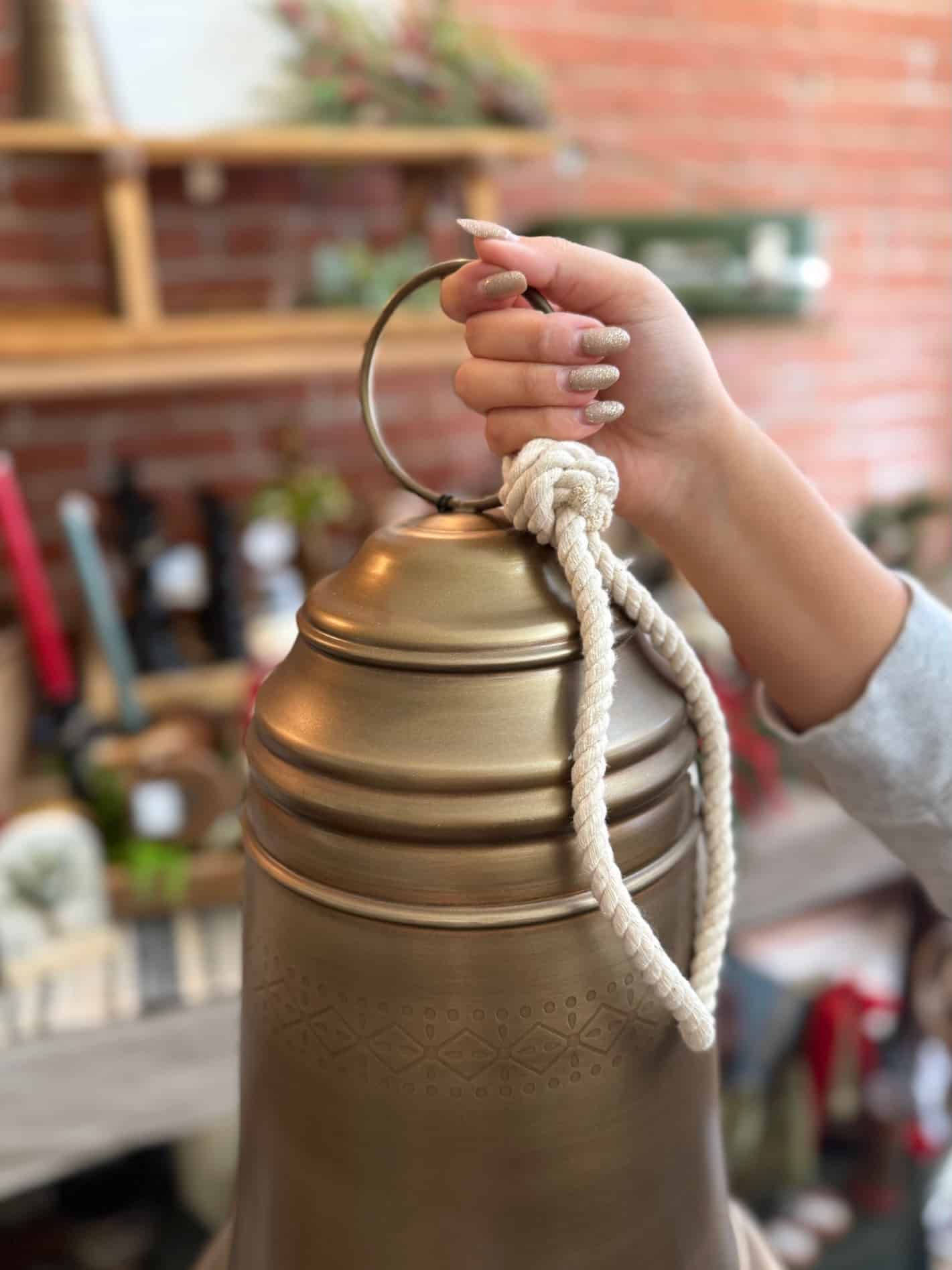 Close-up of the Antique Brass Bell Large being held by its braided rope hanger.