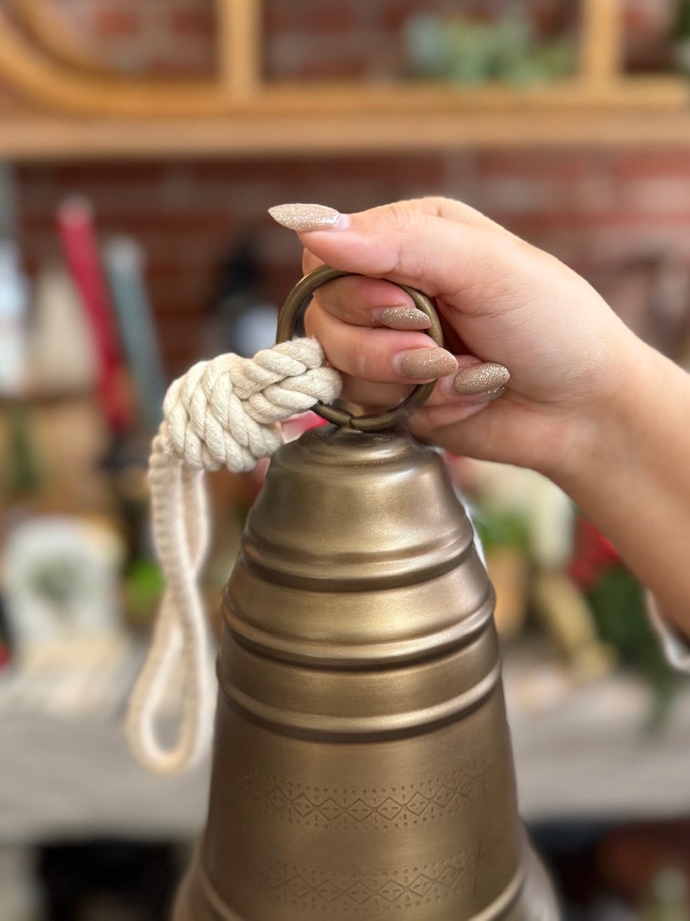 Close-up of the Antique Brass Bell Small being held by its braided rope hanger.