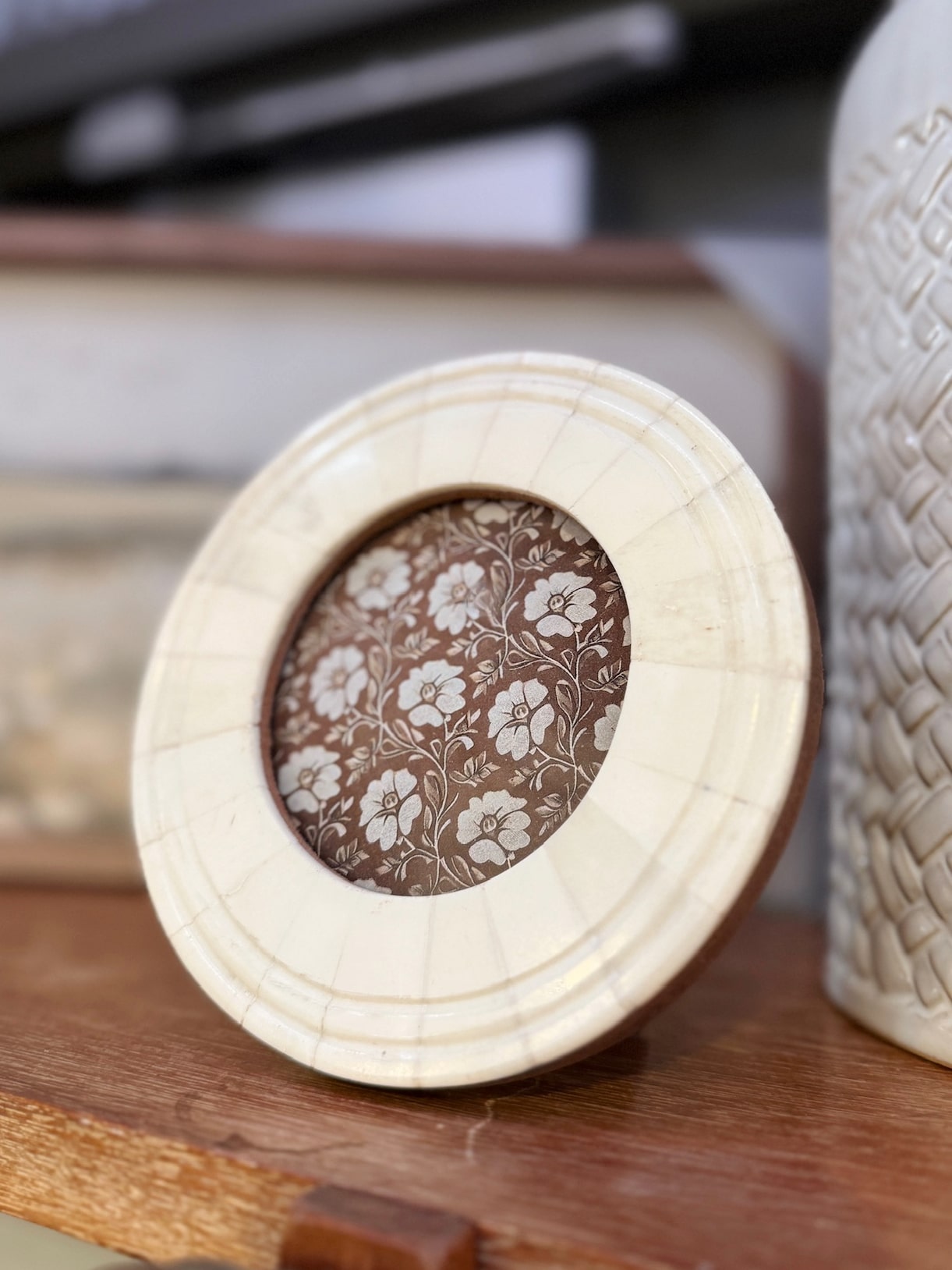 Hand-carved round bone picture frame featuring a floral insert, displayed on a wooden surface.