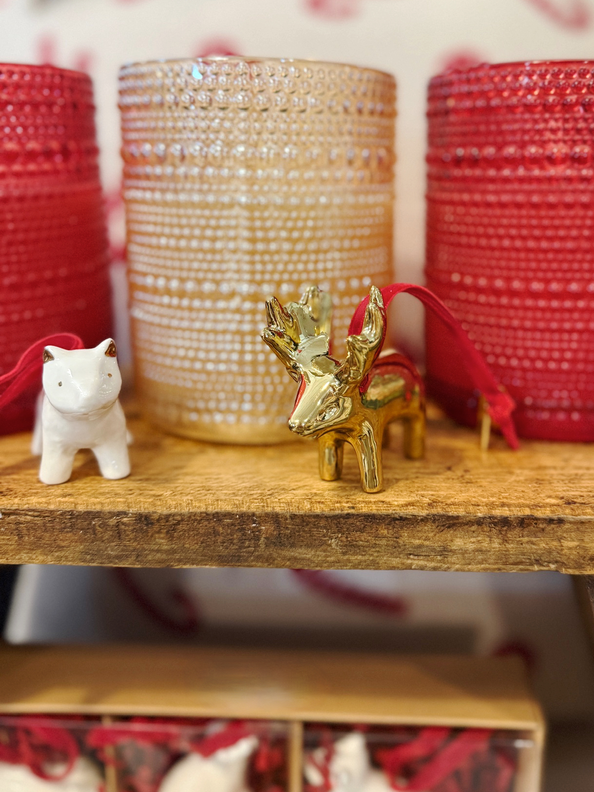 White ceramic fox ornament and gold moose ornament displayed on a wooden shelf with red and gold holiday accents.