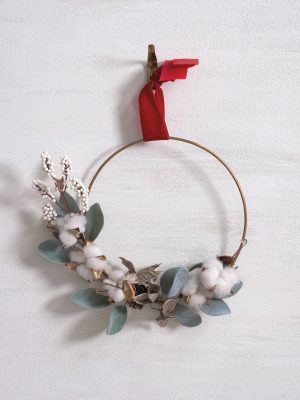 Minimal gold wreath ring decorated with frosted greenery, cotton accents, white berries, and a velvet ribbon for hanging.