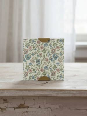 Front view of the Scallop Photo Frame 5x5 with a floral patterned insert and warm gold corner clips, standing on a rustic wood tabletop.