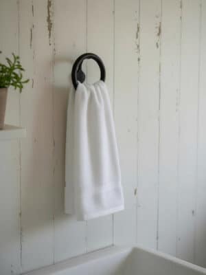 White hand towel hanging from a matte black round metal wall hook on a white paneled wall.