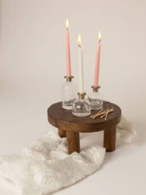 Round wood pedestal styled with skinny taper glass candle holders and pink and ivory taper candles, with matches and soft fabric accents.